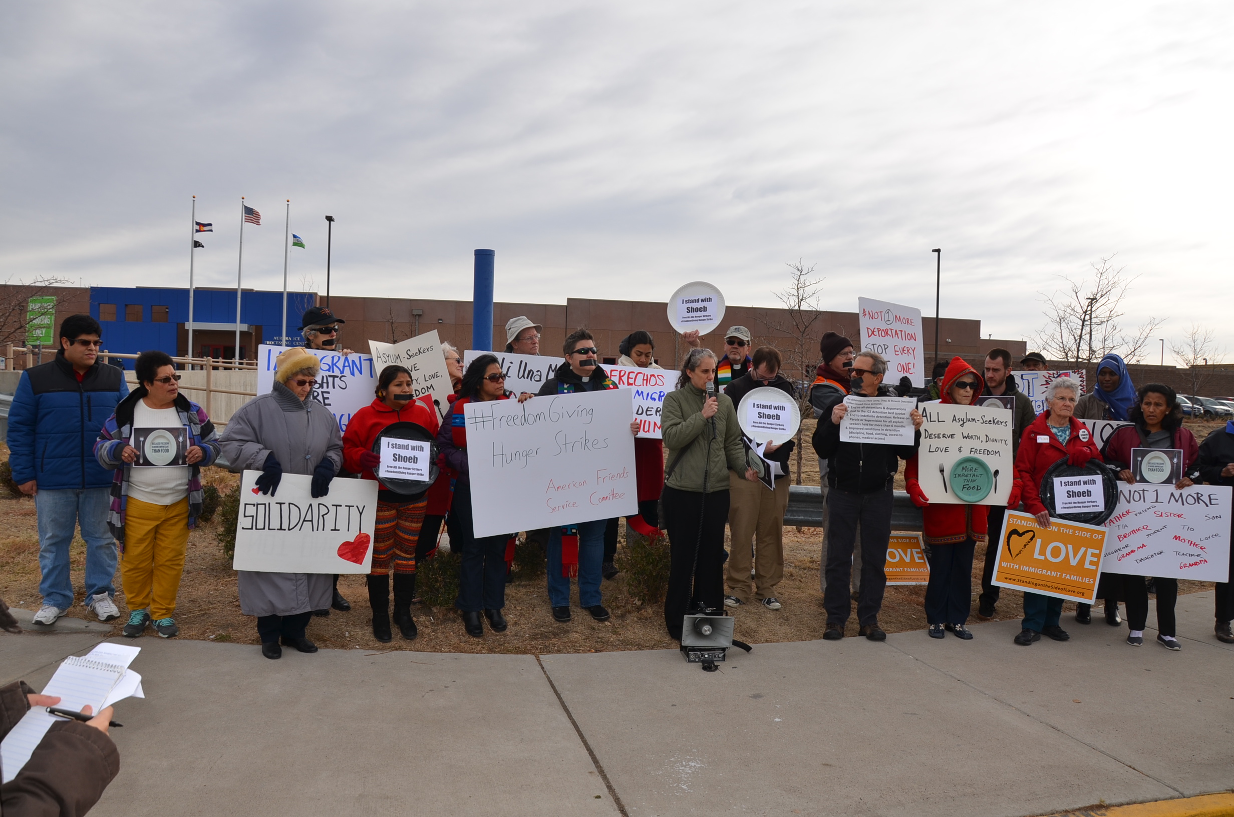 Demonstrators with the American Friends Service Committee use black tape over their mouths and empty plates to protest against the conditions inside the Aurora facility, where between one and four people are still on hunger strike. 