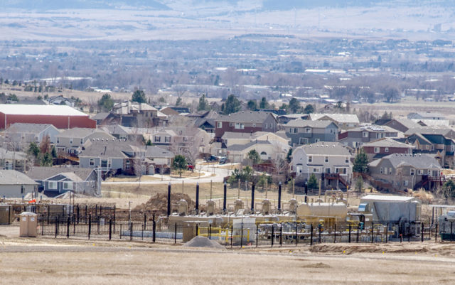 fracking oil and gas well fenced in suburban neighborhood with trees and mountains in the background. Erie Colorado